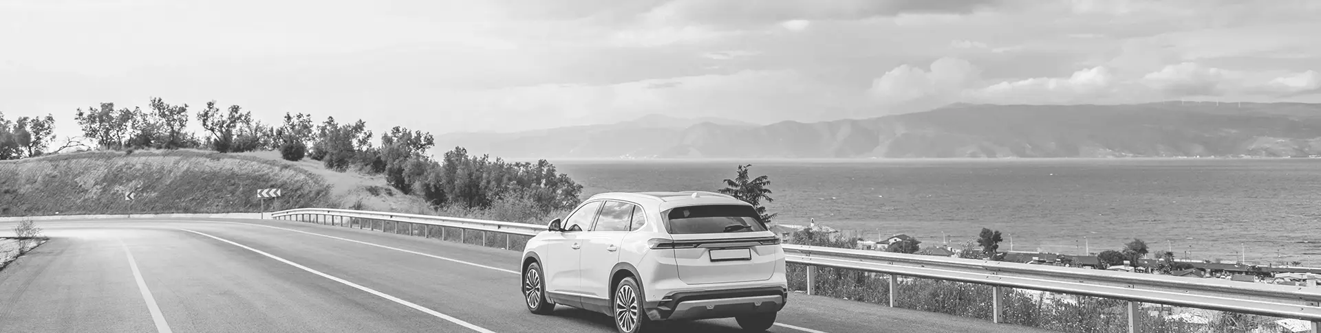 A white SUV driving on a road with water in the background. 